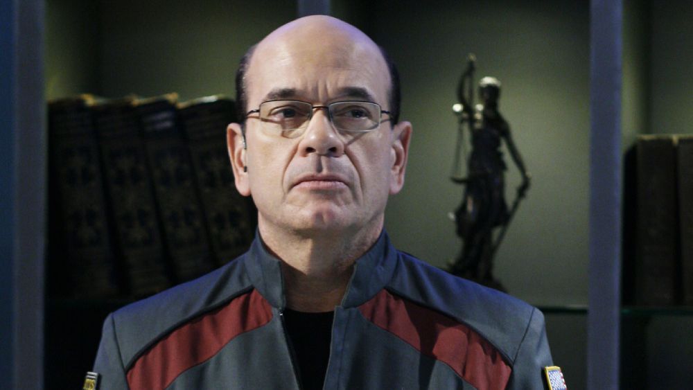 Richard Woolsey (Robert Picardo) sits in his office with his lips pursed.