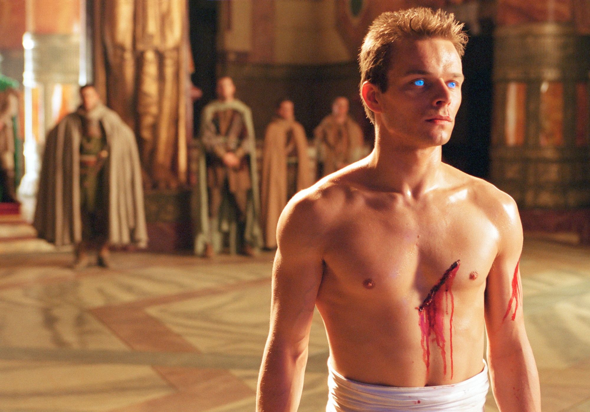 Paul Atreides (Alec Newman) stands in a throneroom, naked from the waist with a bleeding cut across his left breast.