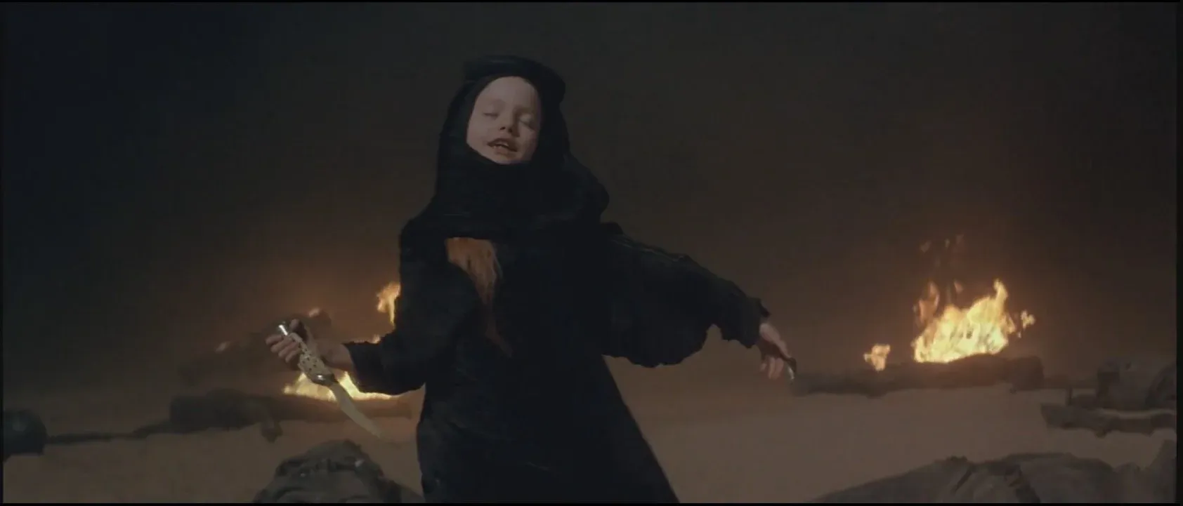 Alia Atreides (Alicia Witt) dances with her dagger, flames visible in the background. She is wearing a black hijab.
