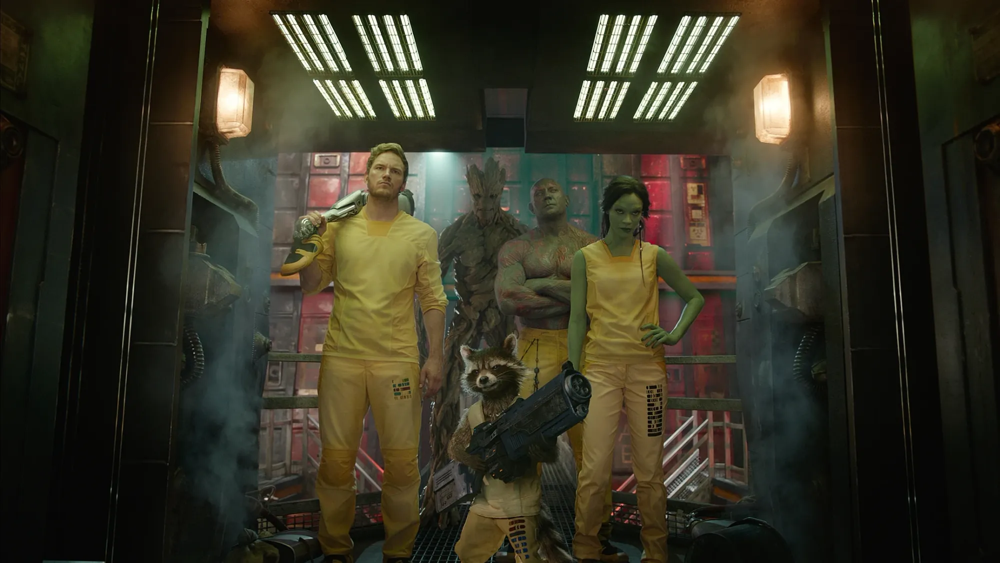 Star-Lord (Chris Pratt), Groot (Vin Diesel), Rocket (Bradley Cooper), Drax (Dave Bautista), and Gamora (Zoe Saldana) stand in a doorway in yellow prison uniform.