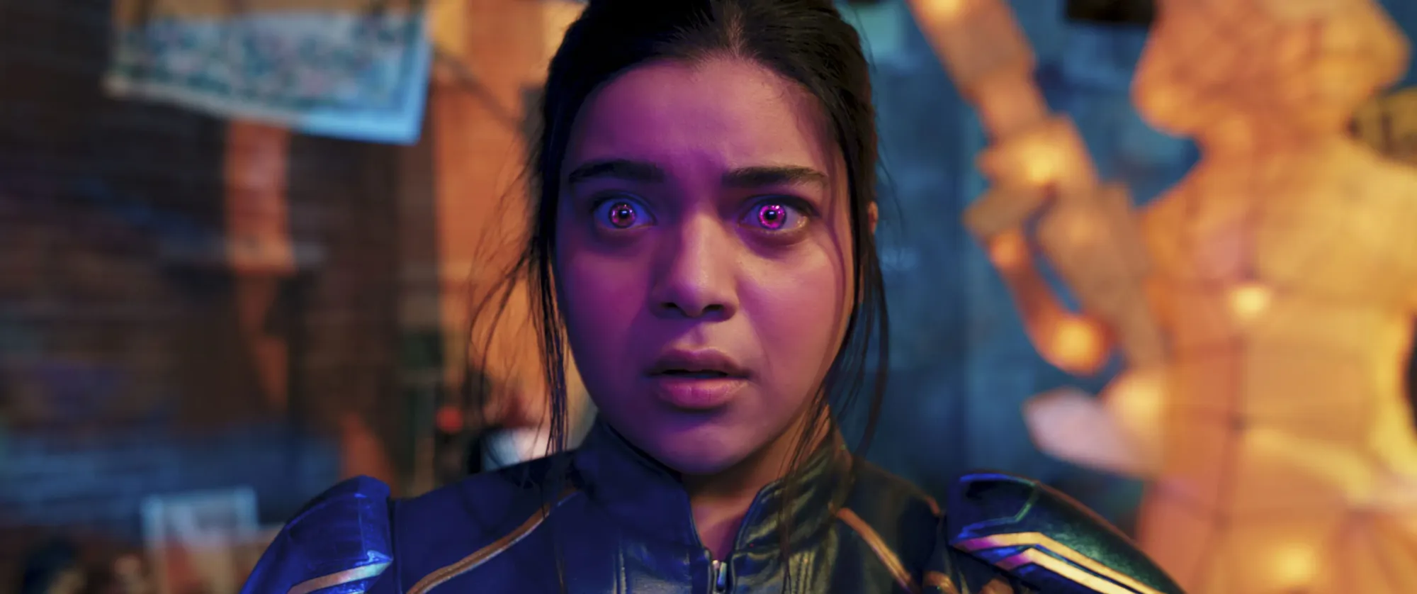 Kamala Khan (Iman Vellani) wearing a Captain Marvel costume, her eyes glow pink-purple.