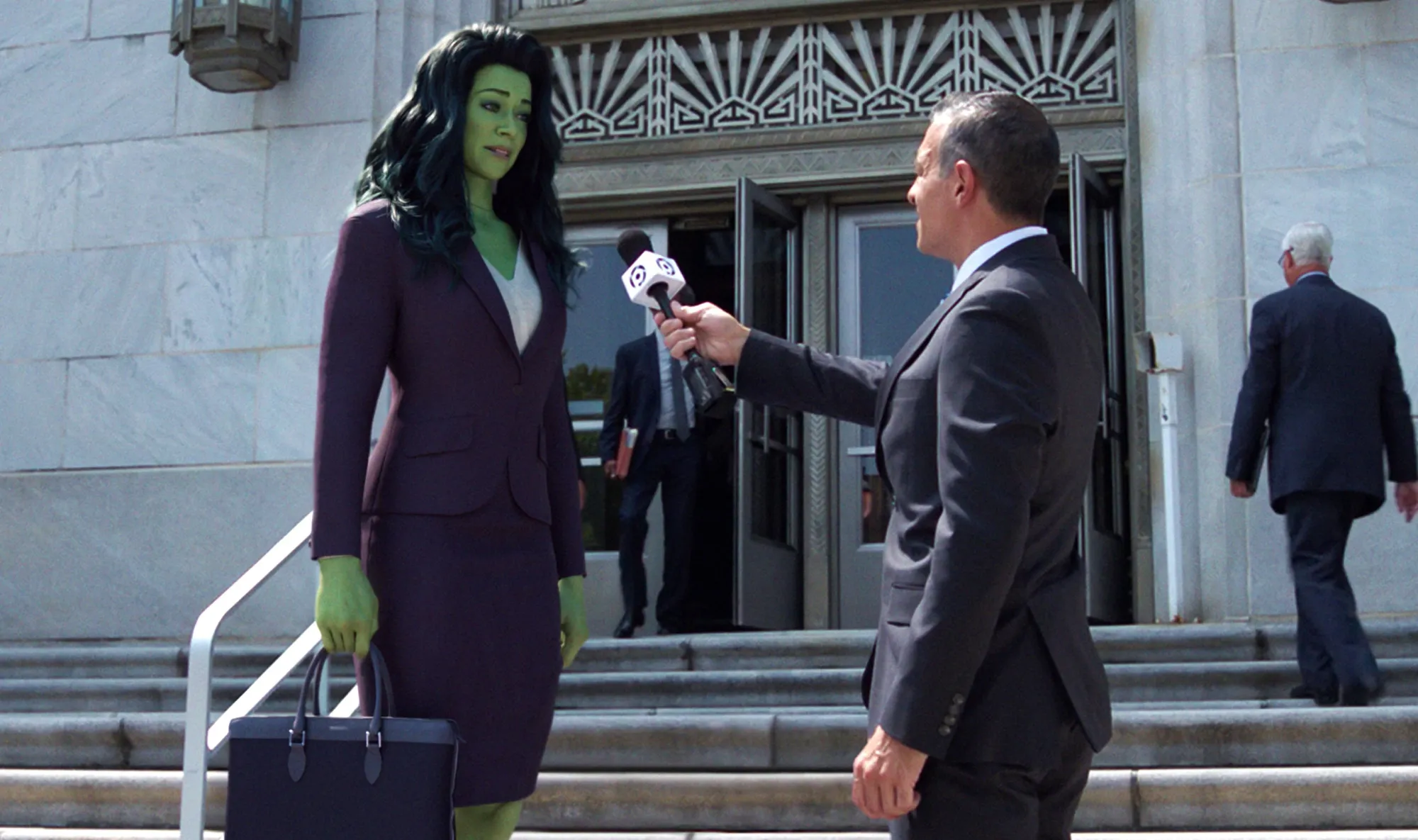 Jennifer Walters (Tatiana Maslany) stands on the courthouse steps speaking to a news reporter with a microphone.