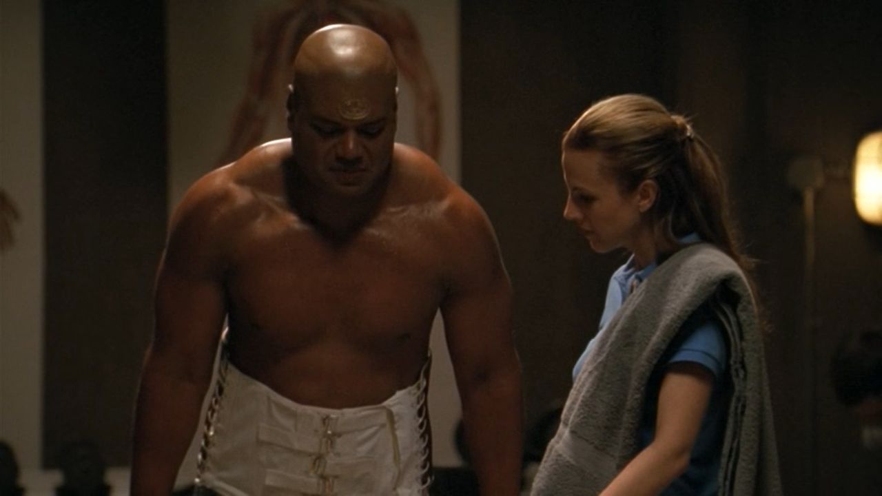 Teal'c (Christopher Judge) is shirtless as he attempts to walk, a physio stands watching him with a towel over her shoulder.