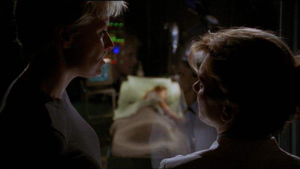 Samatha Carter (Amanda Tapping) and Janet Frasier (Teryl Rothery) talk, Cassandra visible through the glass in front of them.