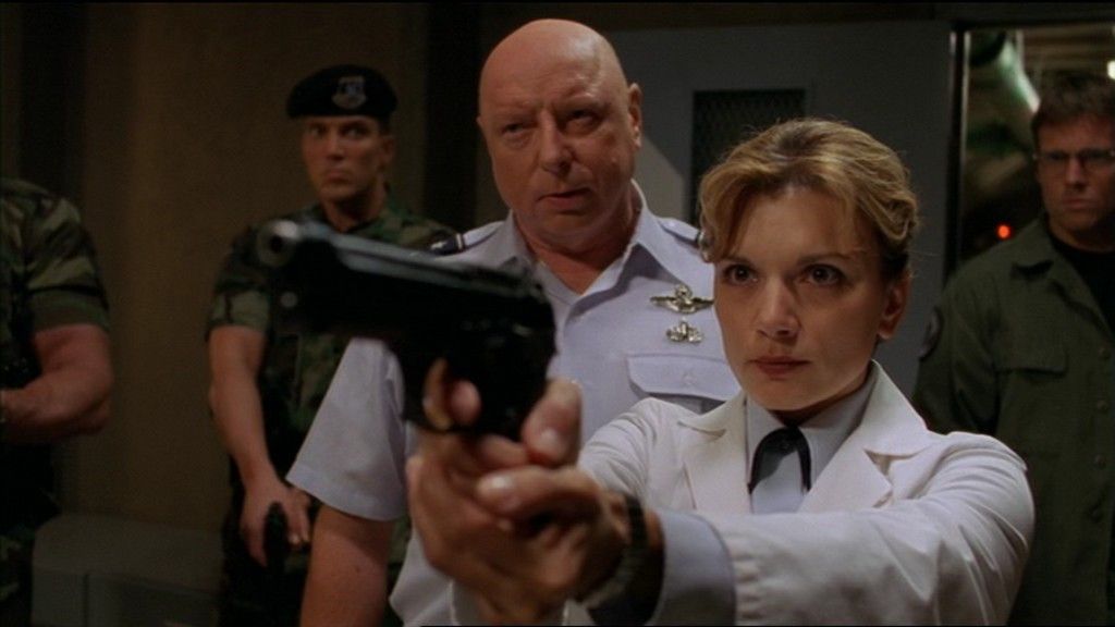 Janet Frasier (Teryl Rothery) stares down the barrel of a sidearm, General Hammond (Don S. Davis) behind her.