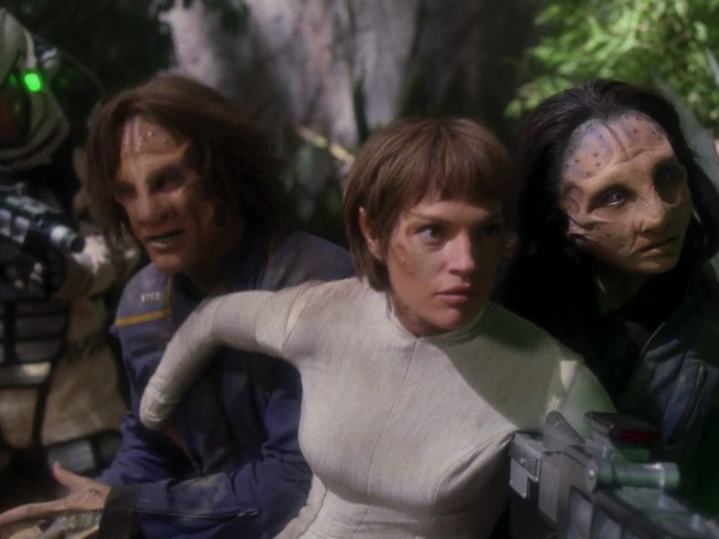 A mutated Archer (Scott Bakula) and Hoshi (Linda Park), their faces obscured by ridges on their brows and noses, shelter behind T’Pol (Jolene Blalock) who has a subtle ridfe on her face.