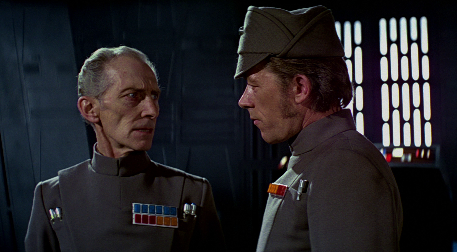 Grand Moff Tarkin (Peter Cushing) turns his head to speak to another Imperial officer.