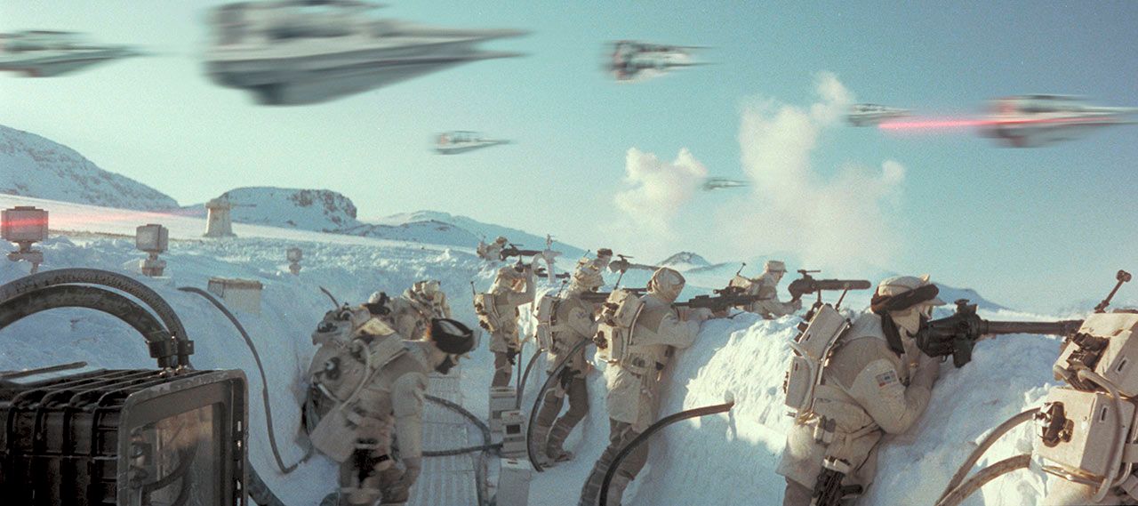 Rebel speeders fly over a trench in which white-clad Rebel troopers aim their guns.