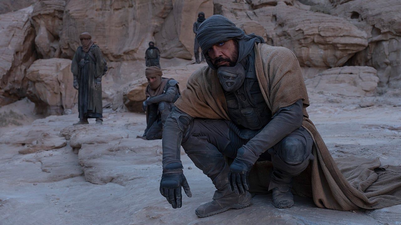 Stilgar (Javier Bardem) squats on a rock, with the Fremen behind him.