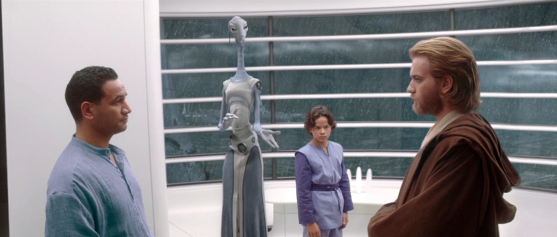 Jango Fett (Temuera Morrison), Tuan We (Rena Owen), Boba Fett (Daniel Logan), and Obi-Wan Kenobi (Ewan McGregor) speak on Kamino. The churning ocean can be seen through the window behind them.