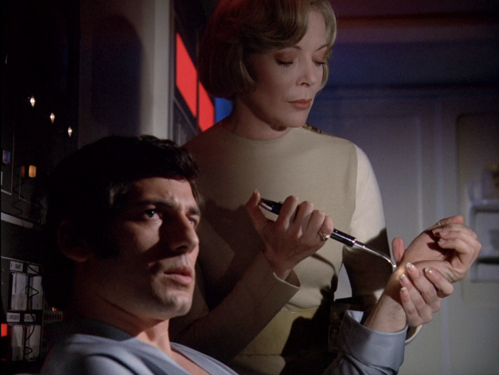  Helena Russell (Barbara Bain) holds a glowing pen-like device to Dr. Dan Mateo (Giancarlo Prete)'s wrist as he looks up at something out of shot..