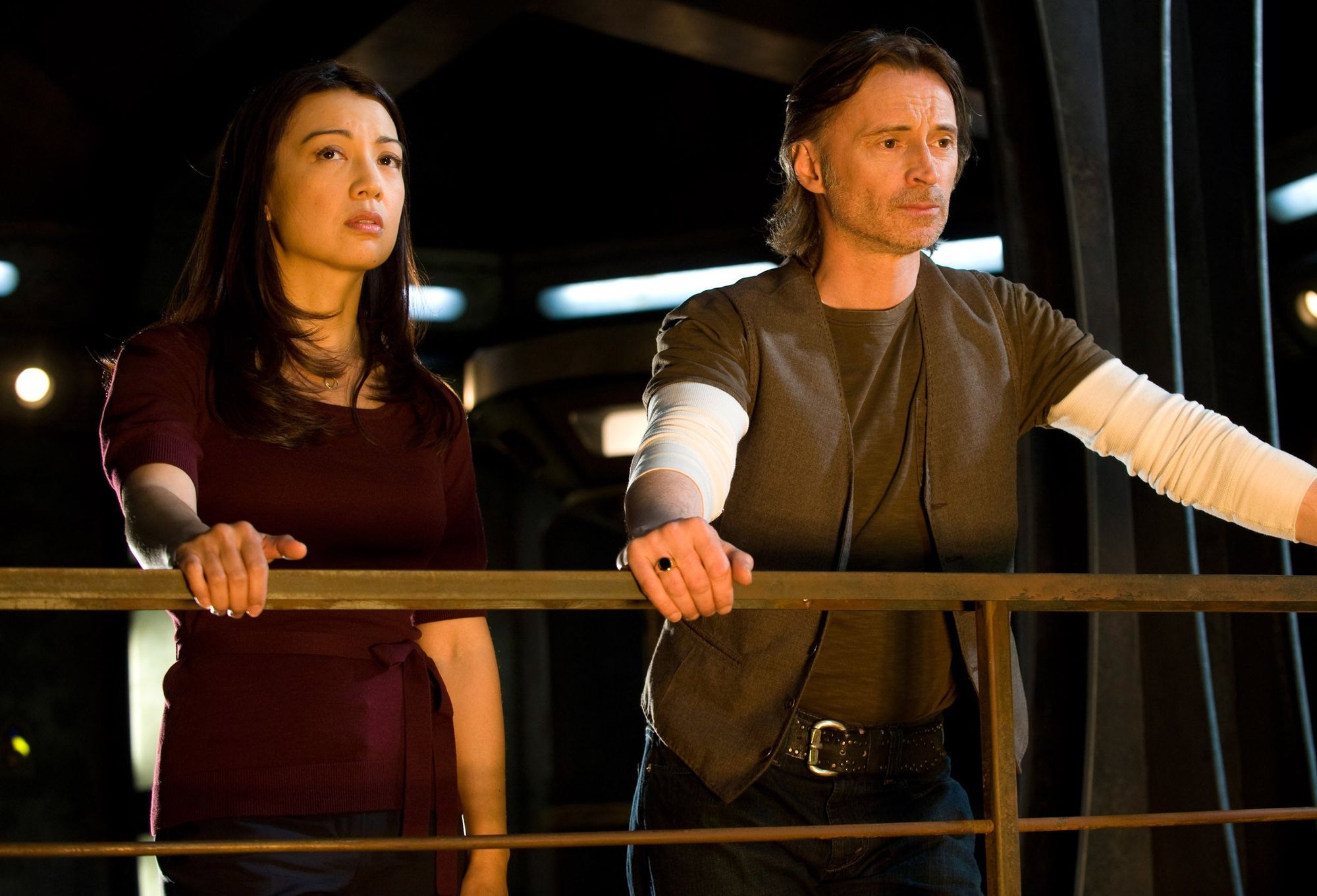 Camile Wray (Ming-Na Wen) and Nicholas Rush (Robert Carlyle) stand side by side, behind a rail.