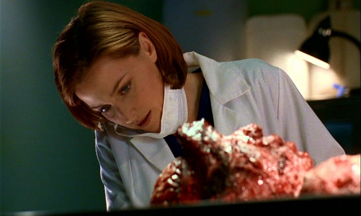 Dana Scully (Gillian Anderson) leans over Simon de la Cruz (Luis Villalta)’s body.