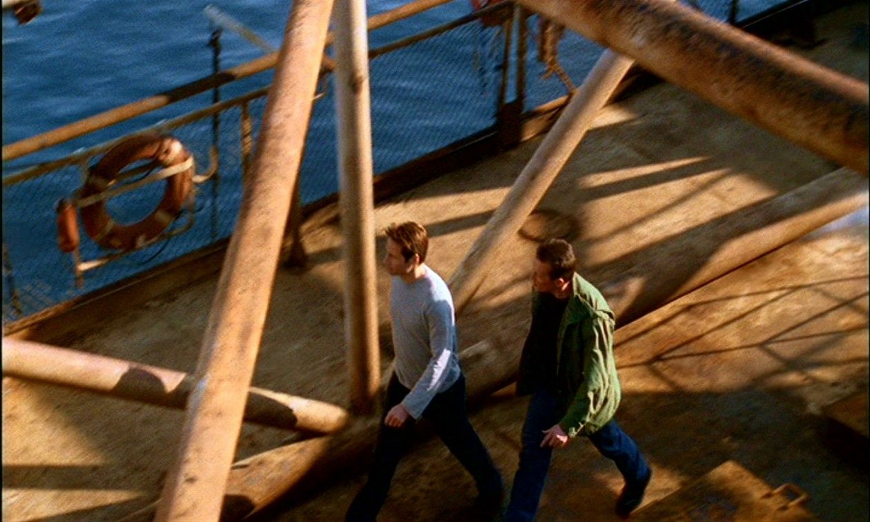 John Doggett (Robert Patrick) and Fox Mulder (David Duchovny) viewed from above as they walk across the rusted deck of an oil rig.