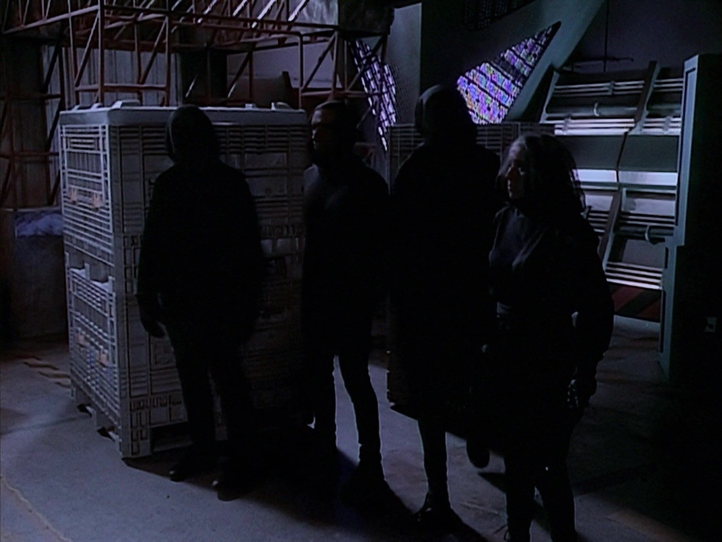 Four black clad figures lurk next to containers.