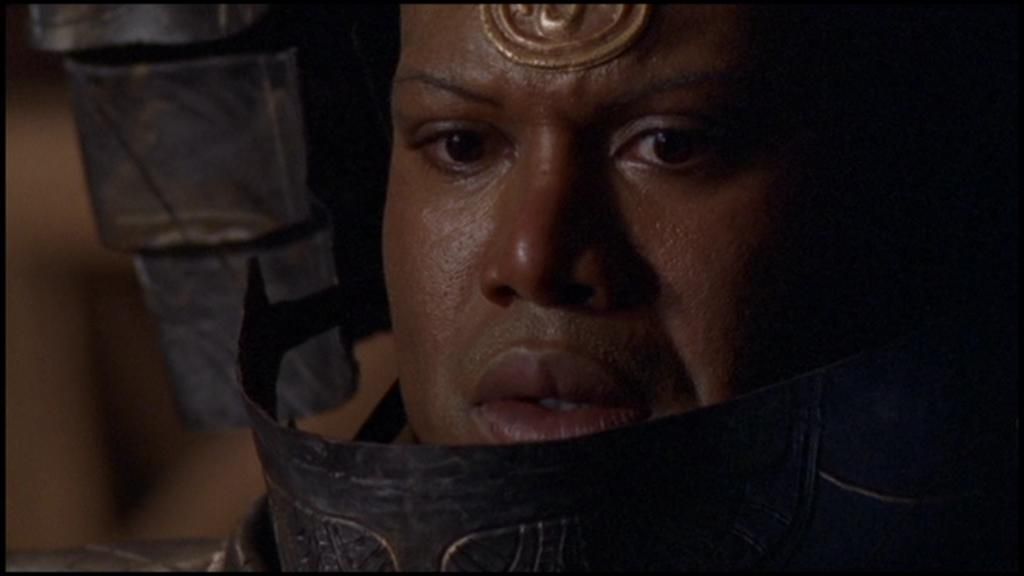 Teal'c, wearing his Serpent Guard, armour, looks down at his victim. His helmet is open, revealing an expression of horror.