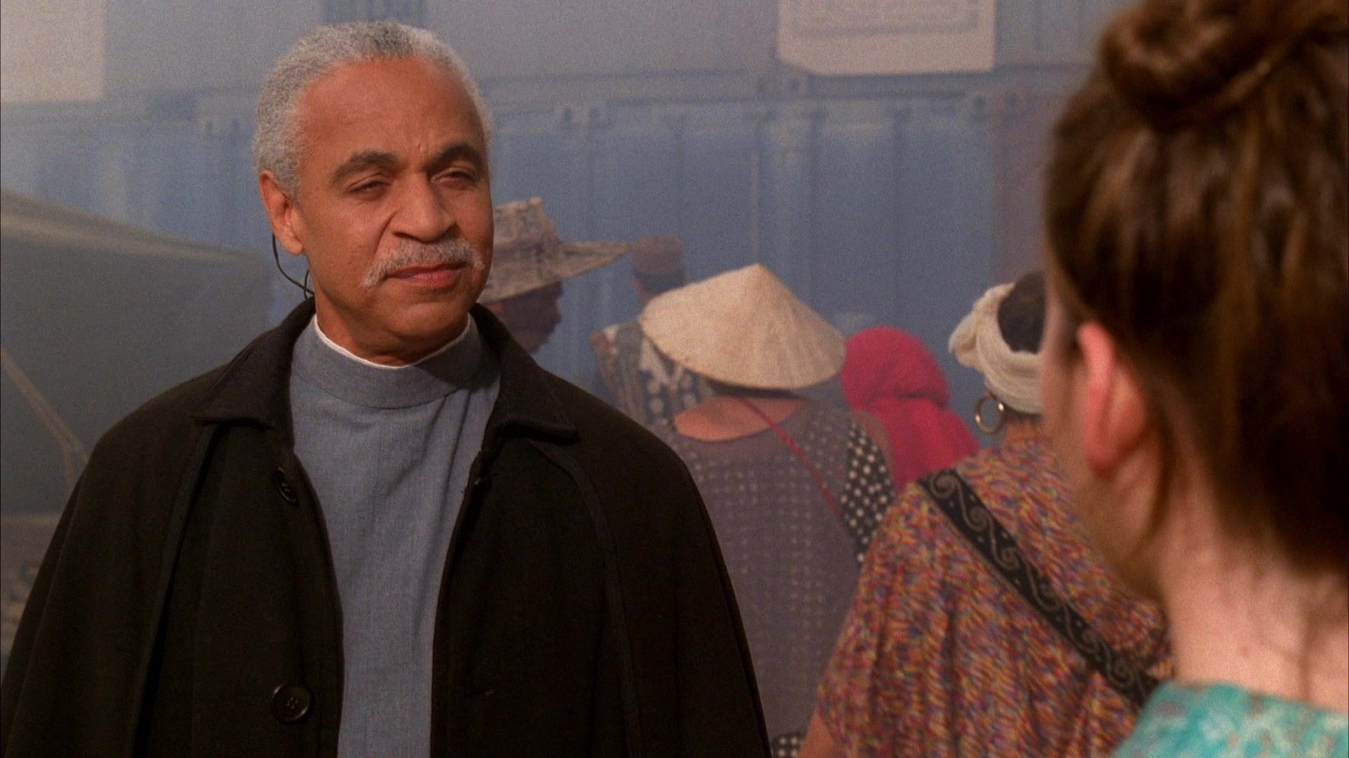 Shepherd Book (Ron Glass) meets Kaylee Frye (Jewel Staite) in the Firefly episode ‘Serenity’. The two are outside in a busy market setting.