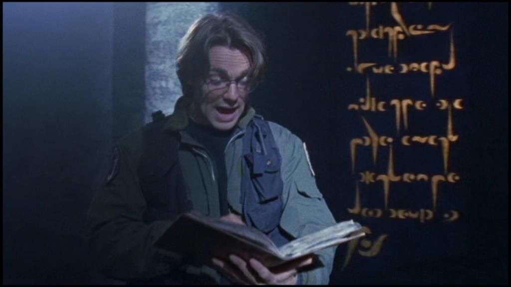 Daniel Jackson (Michael Shanks) reads aloud from a book as alien text glows on the wall behind him.