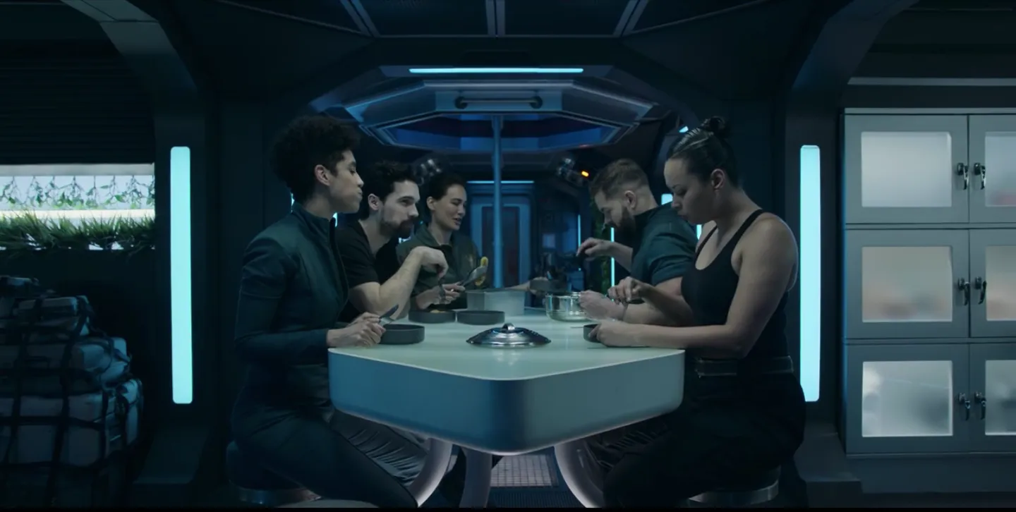 The crew of Rocinante sit around the galley table for a meal. From left to right they are Naomi Nagata, James Holden, Clarissa Mao, Amos Burton, and Bobbie Draper.