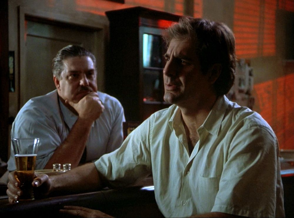 Al (Bruce McGill) listens to Sam Beckett (Scott Bakula) who sits at the bar.