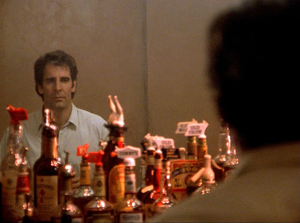 Dr. Sam Beckett (Scott Bakula)'s reflection is visible at the back of the bar.