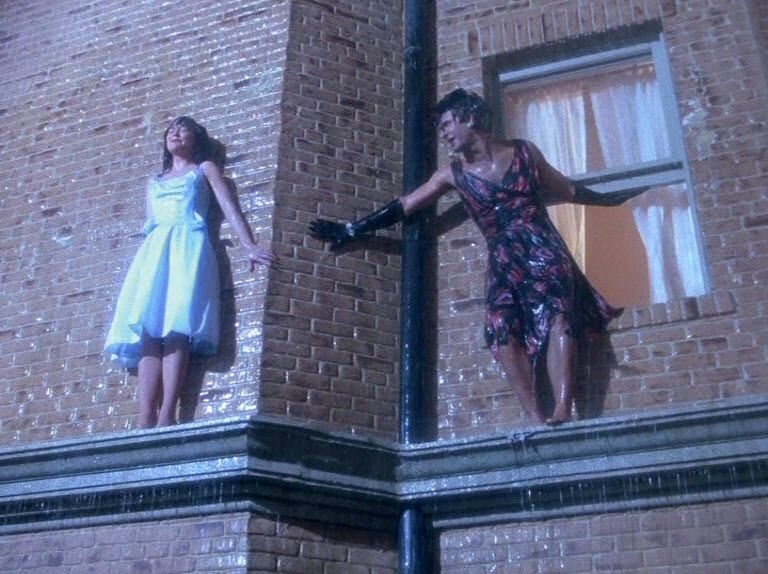 Gloria Collins (Jean Sagal) stands on a building ledge in the rain.