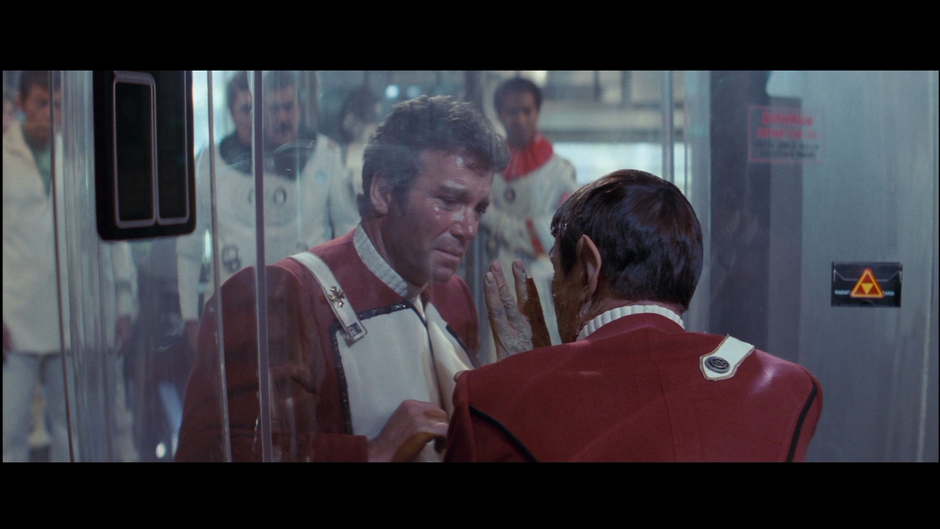 Captain Kirk, played by William Shatner, and Spock, played by Leonard Nimoy, in the movie Star Trek II: The Wrath of Khan. Spock, whose skin is peeling makes his iconic Vulcan salute against the glass that divides the two men.