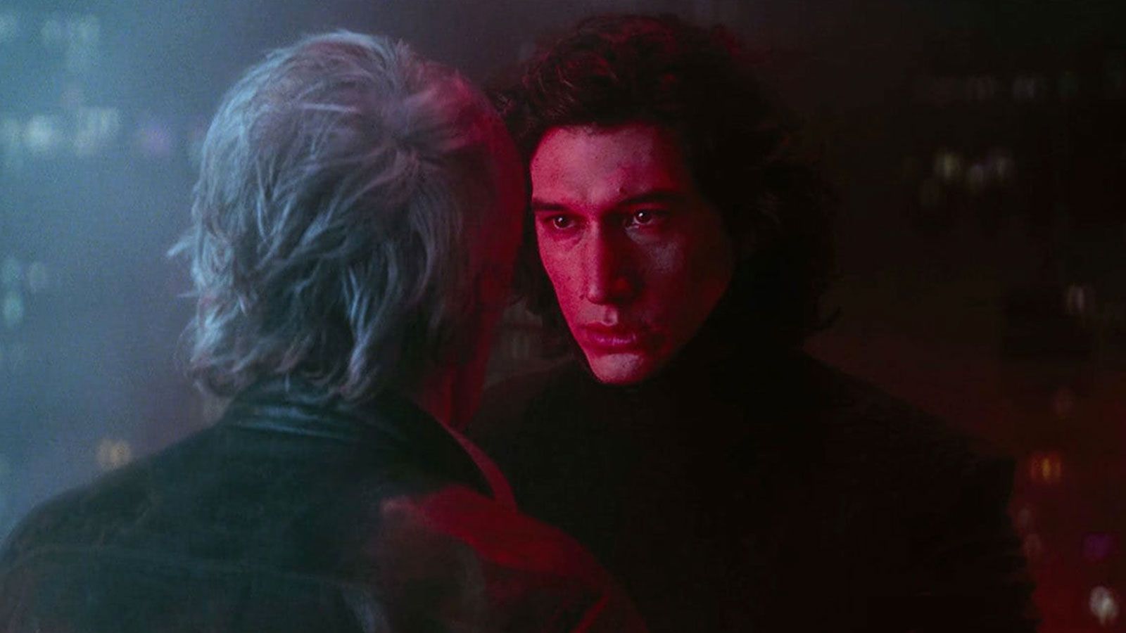 Kylo Ren (Adam Driver)'s face is bathe in the red light of his lightsaber as he faces Han Solo (Harrison Ford).