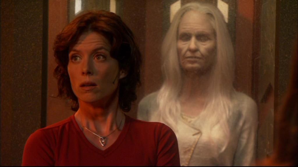 Elizabeth Weir (Torri Higginson) stands in front of the stasis chamber containing her aged counterpart.