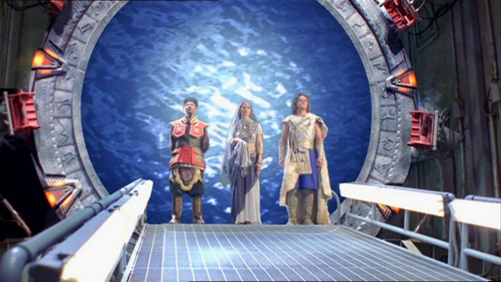 The System Lords Yu, in traditional Chinese dress, Nirrti, in Middle Eastern dress, and Cronus in Greco-Roman-inspired clothes, stand at the top of the ramp in the Gate Room.