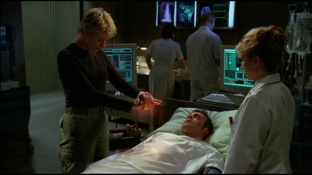 Samantha Carter (Amanda Tapping) holds a glowing device over the prone Daniel Jackson (Michael Shanks)