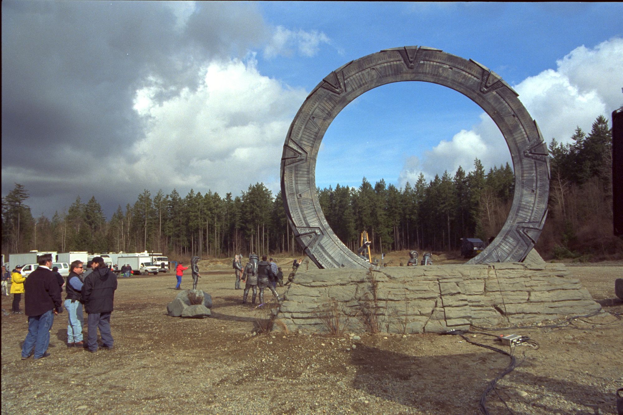 Cast and crew swarm around an outside Stargate with base. A spotlight is positioned in the middle of the gate to create the glare when it activates for Stargate SG-1 episode ‘Need’.