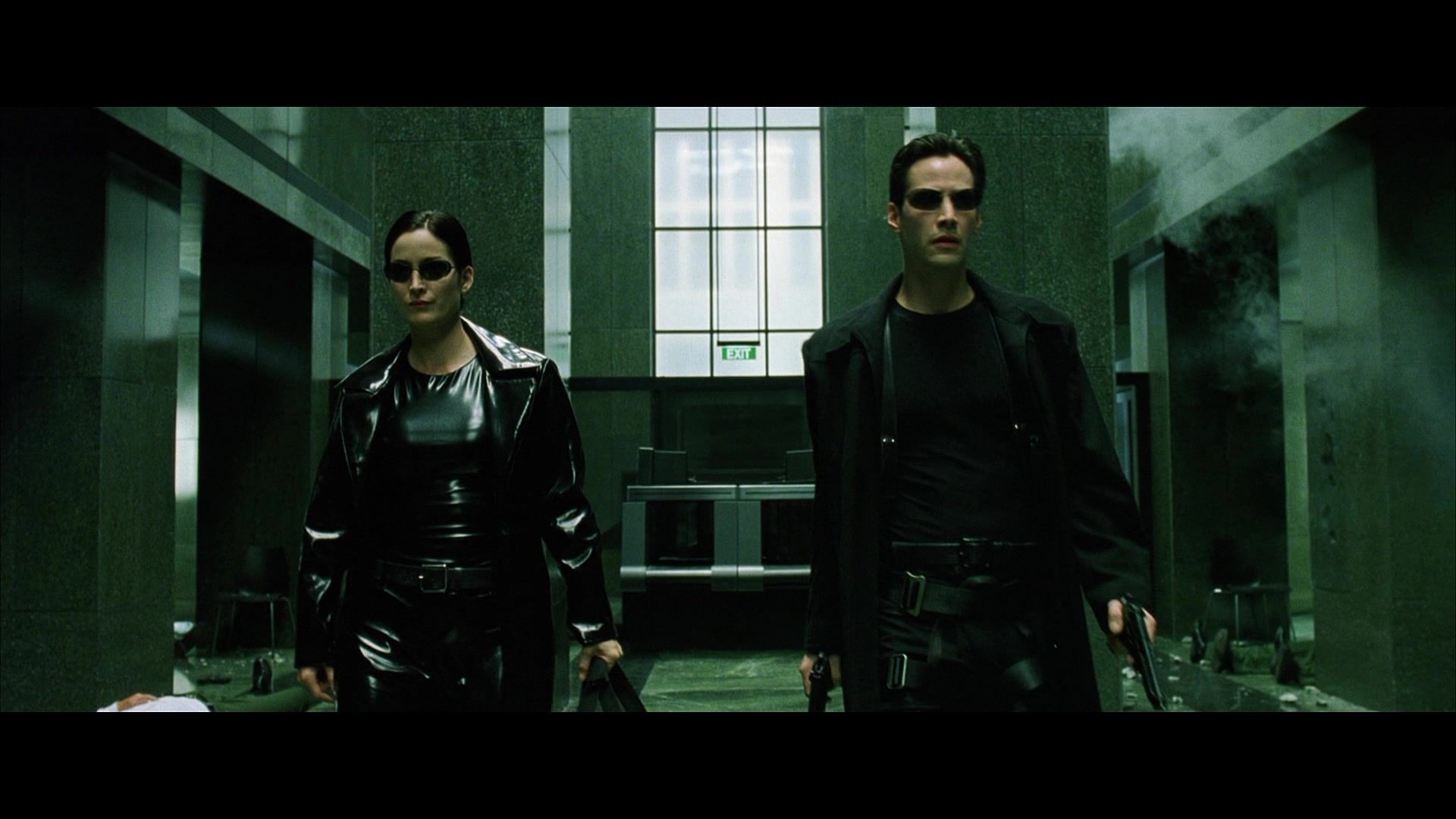 Trinity (Carrie-Anne Moss) and Neo (Keanu Reeves) walk towards the camera.