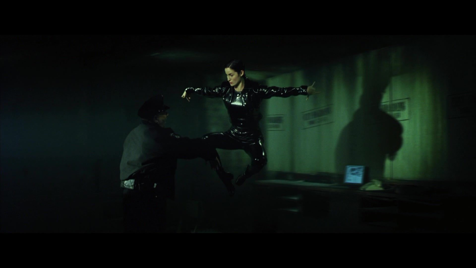 Trinity (Carrie Anne Moss) sits in the dark with her back to the camera.
