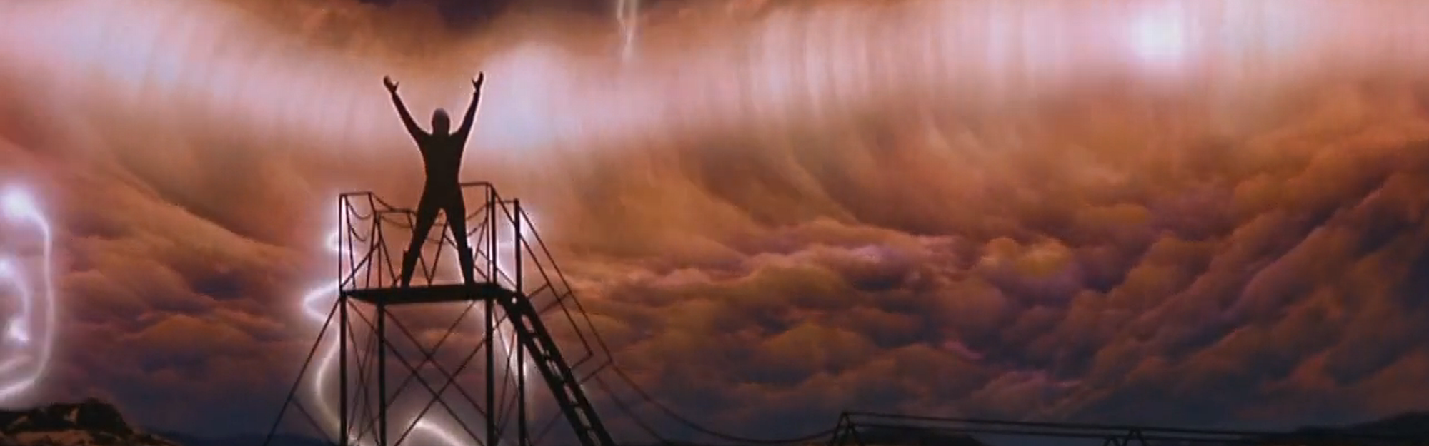 Tolian Soran raises his arms as a ribbon of energy tears across the sky behind him.