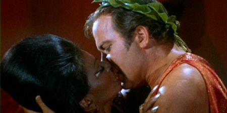 Kirk embraces Uhura. He is wearing a glittery toga and laurels.