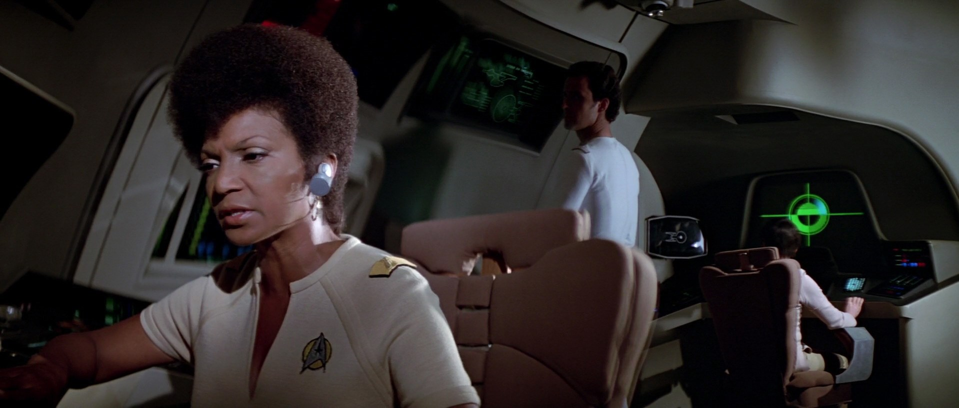 Uhura wearing a pale brown uniform sits at the communications station.
